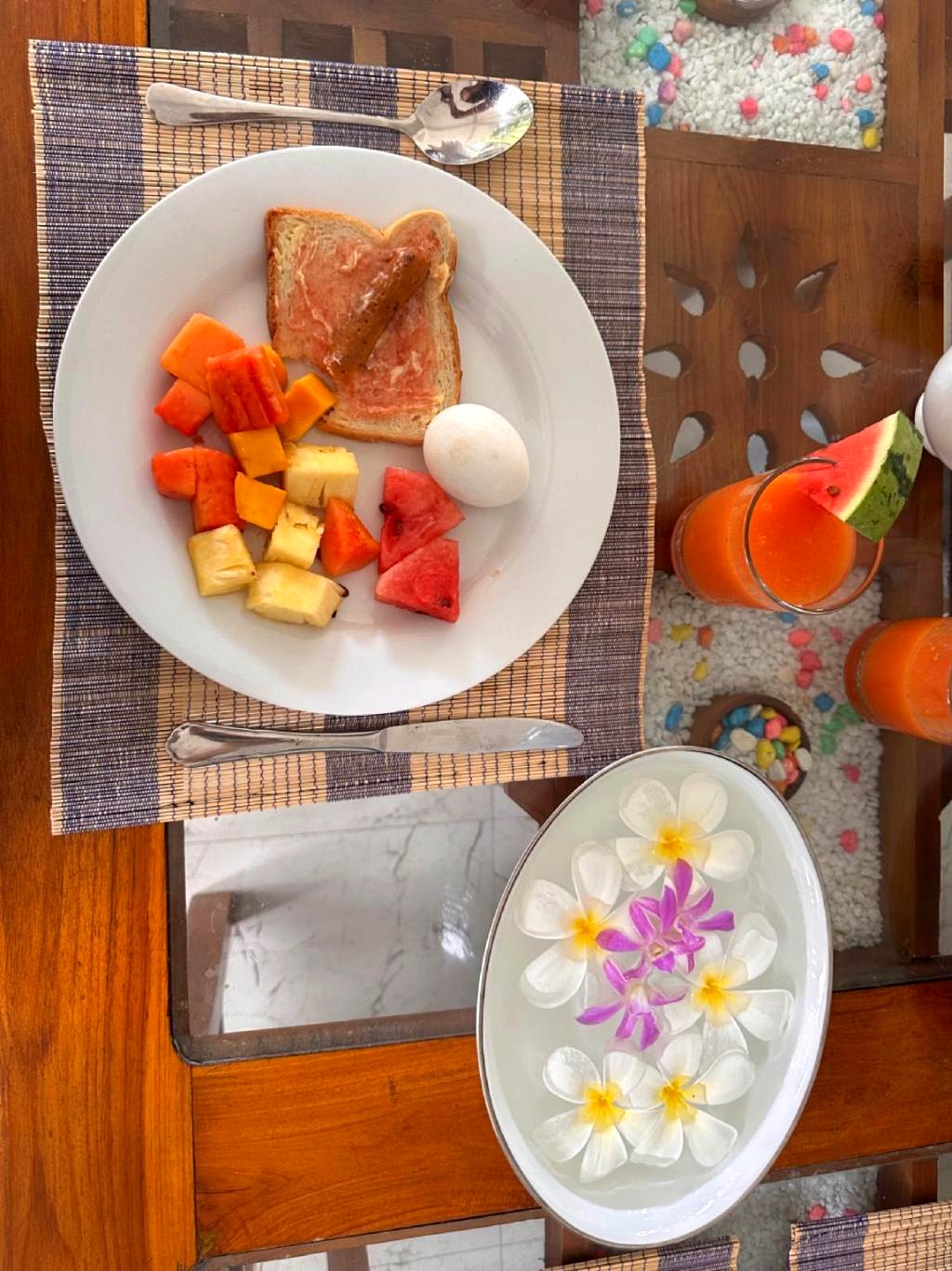 Villa Estuary breakfast — fresh tropical fruit, egg, toast, fresh juice and frangipani flowers